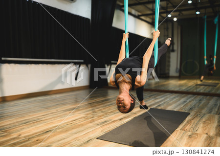 Young woman practicing aerial yoga upside down using blue hammock in fitness studio Young woman practicing aerial yoga upside down using blue hammock in fitness studio 130841274
