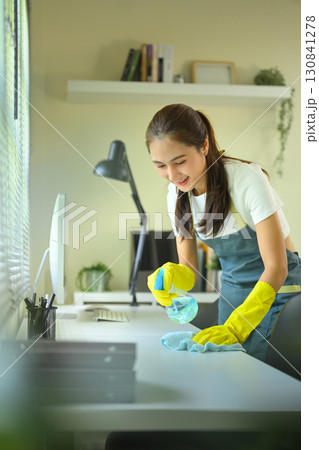 Smiling woman disinfecting desk with spray cleaner and cloth in office, concept of hygiene and sanitation Smiling woman disinfecting desk with spray cleaner and cloth in office, concept of hygiene and sanitation 130841278