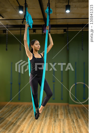 Young African woman practicing aerial yoga using blue hammock in fitness studio Young African woman practicing aerial yoga using blue hammock in fitness studio 130841315