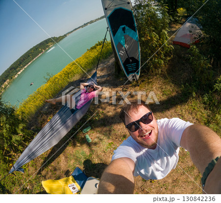 Couple Enjoying Lakeside Camping with Paddleboard Couple Enjoying Lakeside Camping with Paddleboard 130842236