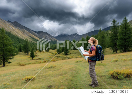 Hiker with backpack holding map in green mountain valley under dramatic cloudy sky, enjoying nature and adventure outdoors 130843055