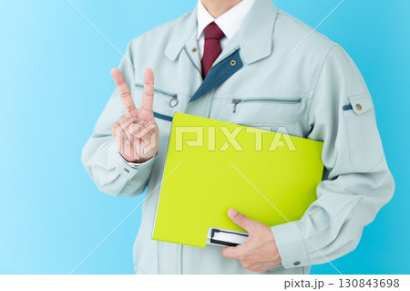 バインダーを持って2本指を立てる作業着姿のミドル男性ビジネスマン バインダーを持って2本指を立てる作業着姿のミドル男性ビジネスマン 130843698