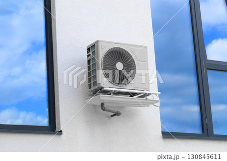 Condenser unit or compressor outside of residential building. Unit of central air conditioner AC or heating ventilation air conditioning system HVAC. Electric fan AC hangs on the wall 130845611