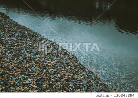 A tranquil scene - a shoreline of stones meeting calm waters of a river. Abstract view of the edge of a body of water, with a diagonal separating line A tranquil scene - a shoreline of stones meeting calm waters of a river. Abstract view of the edge of a body of water, with a diagonal separating line 130845894
