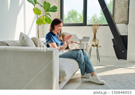 Young woman looking at laptop screen talking having video call sitting on couch at home 130846053
