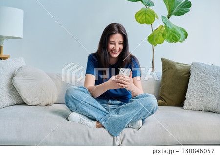 Young happy woman sitting at home on the couch using a smartphone 130846057