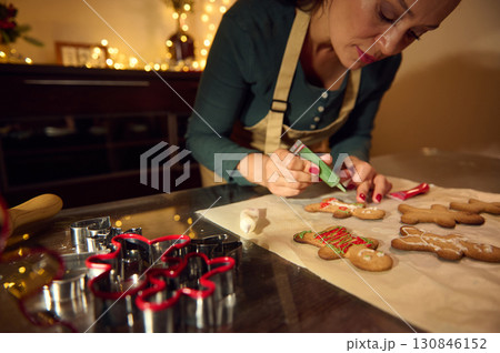 Woman Icing Gingerbread Cookies in Cozy Holiday Kitchen Setting 130846152