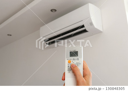 Air conditioner temperature adjustment with remote controller in room at home. Hand holding remote controller of air conditioner inside the white room and set at cool temperature 130848305