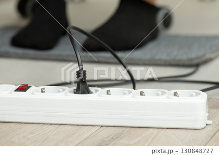 Close up of electric plug of warming mat turned on to the outlet. Warming foots while working on the computer Close up of electric plug of warming mat turned on to the outlet. Warming foots while working on the computer 130848727