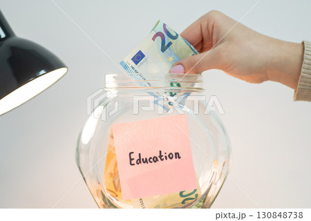 Putting euro money into glass jar with Education inscription. Concept of saving up for education in Europe 130848738