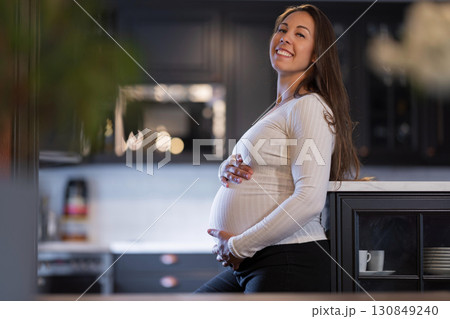 Smiling pregnant woman enjoying a quiet moment in a modern kitchen setting Smiling pregnant woman enjoying a quiet moment in a modern kitchen setting 130849240