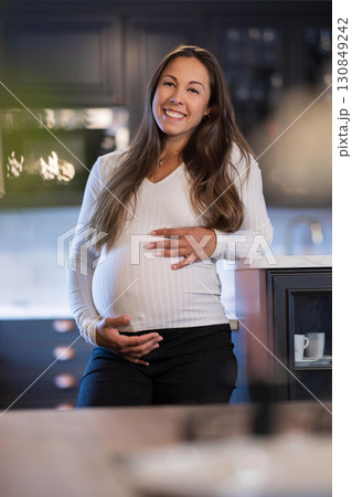 Smiling pregnant woman standing in modern kitchen with positive energy 130849242