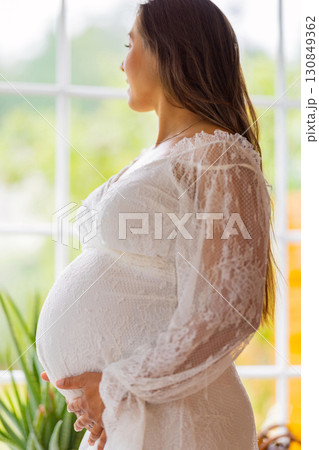 Pregnant Woman in White Dress by a Bright Window, Anticipating Motherhood 130849362