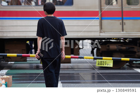 夏の都市の街の踏切で待つ男性と通過中の電車の様子 130849591