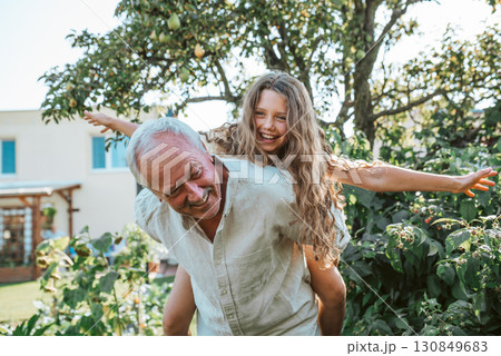 Grandfather playing with granddaughter in the garden. 130849683