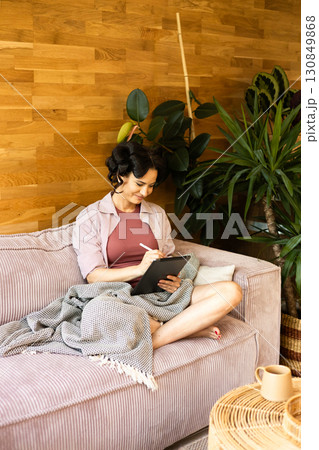 Woman with hair rollers journaling in the morning, using tablet. Woman with hair rollers journaling in the morning, using tablet. 130849868