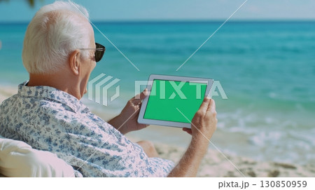Senior man using tablet with blank green screen on tropical beach 130850959