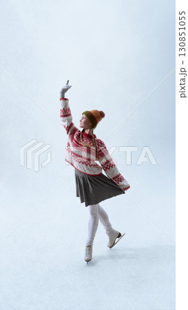 Female figure skater in festive knitwear lifting arm with elegance on ice Female figure skater in festive knitwear lifting arm with elegance on ice 130851055