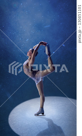 Flexible female skater holding leg in dramatic pose under icy blue spotlight Flexible female skater holding leg in dramatic pose under icy blue spotlight 130851101