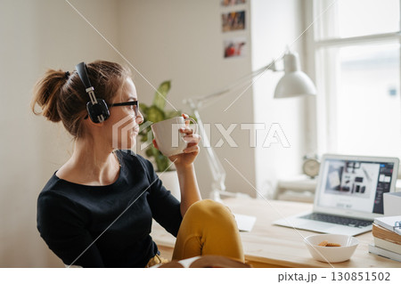Female student taking break during study session, listening music and drinking coffee. Female student taking break during study session, listening music and drinking coffee. 130851502
