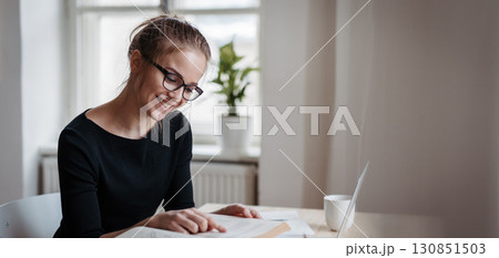 Young female student sitting at the table and studying. 130851503