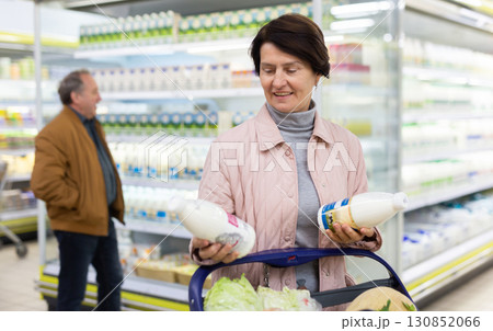 Mature couple choosing jug of milk in dairy department in grocery store 130852066