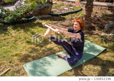 Woman doing a stretching exercise with a wooden stick during outdoor mobility practice. Posture alignment, shoulder opening, and spine flexibility. Woman doing a stretching exercise with a wooden stick during outdoor mobility practice. Posture alignment, shoulder opening, and spine flexibility. 130852196
