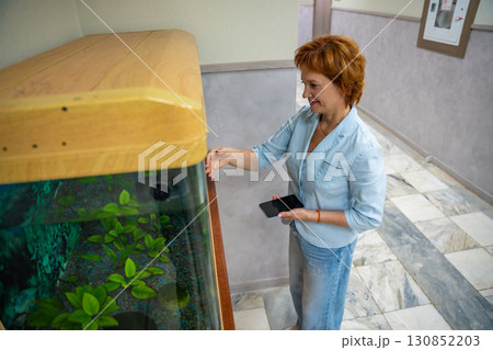 Woman taking a break in the office while watching fish in an aquarium. Stress relief, mindful pause, and mental wellness at the workplace. Woman taking a break in the office while watching fish in an aquarium. Stress relief, mindful pause, and mental wellness at the workplace. 130852203
