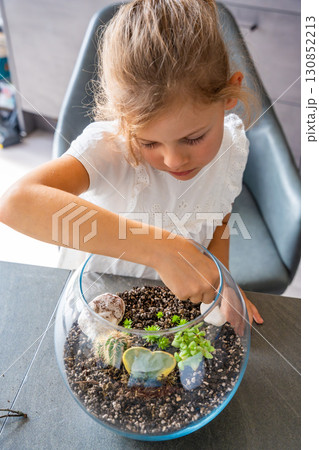 Little girl arranging soil, planting cacti and decorating a terrarium with stones and shells. Concept of creativity, eco-conscious learning and hands-on nature-based activity in childhood Little girl arranging soil, planting cacti and decorating a terrarium with stones and shells. Concept of creativity, eco-conscious learning and hands-on nature-based activity in childhood 130852213