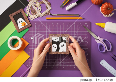 Making a ghost portrait craft. Hands holding the finished craft against a backdrop of craft supplies. Making a ghost portrait craft. Hands holding the finished craft against a backdrop of craft supplies. 130852236