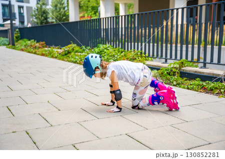 Little girl trying to stand up on roller skates after falling during her first attempts to skate. Persistence, physical development and learning through challenge in early childhood. 130852281