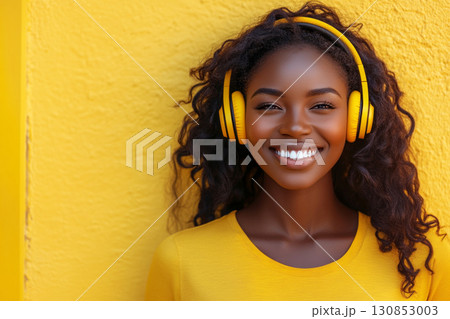 A smiling African American woman with headphones on, set against a vibrant yellow background, captured in clean minimalism, evoking the concept of music enjoyment or learning 130853003