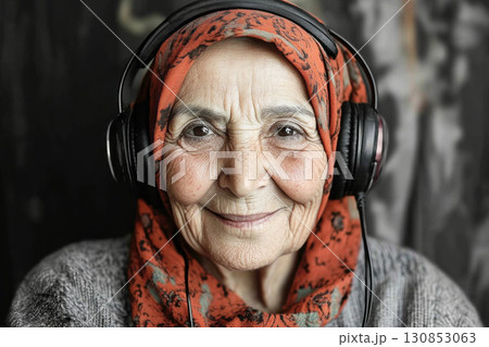 The joyful Arab grandma, wearing headphones, smiles softly with a black and white background, creating a serene, modern minimalist mock-up The joyful Arab grandma, wearing headphones, smiles softly with a black and white background, creating a serene, modern minimalist mock-up 130853063