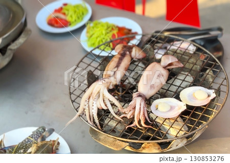 Freshly grilled squid and scallops on mesh grill, with glimpse of street vendor's bustling seaside stall, promise taste of ocean's bounty, authentic local flavors. Street food and seafood concept 130853276