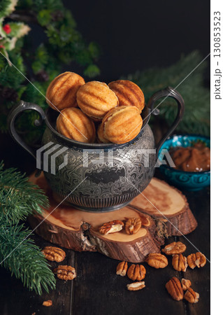 Russian traditional homemade cookies Nuts with condensed milk on an vintage jar on a wooden stand surrounded by spruce branches and scattered nuts. Russian traditional homemade cookies Nuts with condensed milk on an vintage jar on a wooden stand surrounded by spruce branches and scattered nuts. 130853523