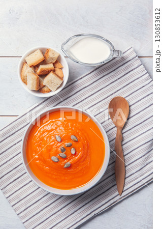 Pumpkin soup-puree with breadcrumbs, cream and seeds on towel, white wooden background 130853612