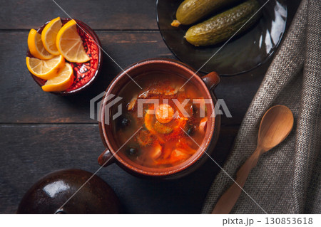 Homemade Traditional Russian soup Solyanka with meat, sausages, vegetables, pickles and olives with lemon in ceramic pot with wooden spoon on dark wooden background, Homemade Traditional Russian soup Solyanka with meat, sausages, vegetables, pickles and olives with lemon in ceramic pot with wooden spoon on dark wooden background, 130853618