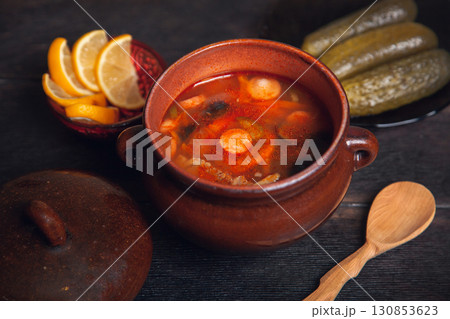 Homemade Traditional Russian soup Solyanka with meat, sausages, vegetables, pickles and olives with lemon in ceramic pot with wooden spoon on dark wooden background Homemade Traditional Russian soup Solyanka with meat, sausages, vegetables, pickles and olives with lemon in ceramic pot with wooden spoon on dark wooden background 130853623