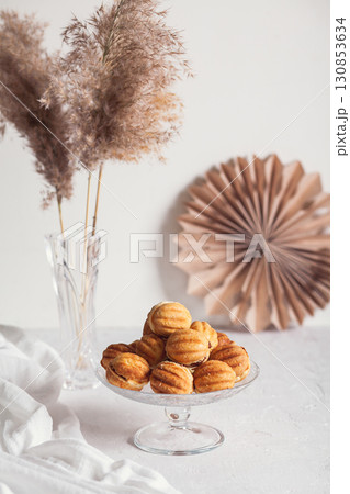 Russian traditional homemade cookies Nuts with condensed milk on glass stand on background of paper decor and reeds in vase White background, selective focus Russian traditional homemade cookies Nuts with condensed milk on glass stand on background of paper decor and reeds in vase White background, selective focus 130853634