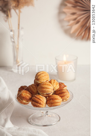 Russian traditional homemade cookies Nuts with condensed milk on glass stand on background of paper decor and reeds in vase and candle White background, selective focus, vertical orientation 130853642