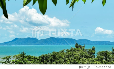 Beautiful seascape with Lush green foliage frames a vibrant blue sea with distant mountains on the horizon, ideal for travel and summer vacation themes, inspiring exploration and relaxation 130853678