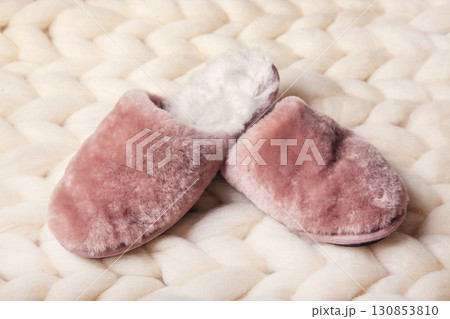 Home slippers made of fur on the background of white merino wool plaid. The atmosphere of homeliness and comfort. 130853810