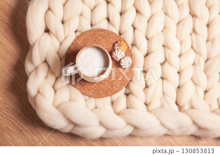 A cup of cappuccino and cookies on the background of blanket of thick yarn. The atmosphere of homeliness and comfort 130853813