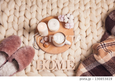 Cup of cappuccino, cookies, candles, cotton plant, home fur slippers, checkered plaid, inscription Home on blanket Cup of cappuccino, cookies, candles, cotton plant, home fur slippers, checkered plaid, inscription Home on blanket 130853819