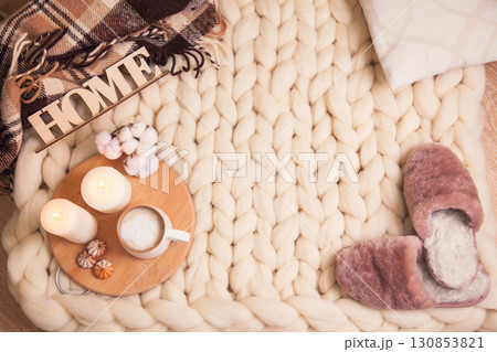 Home fur slippers. cup of cappuccino, candles, checkered plaid, inscription Home on the blanket of thick yarn Home fur slippers. cup of cappuccino, candles, checkered plaid, inscription Home on the blanket of thick yarn 130853821