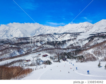 冬の白馬三山を背景にスキーヤーやスノーボーダーが滑るゲレンデ風景 (長野県、白馬、栂池高原) 冬の白馬三山を背景にスキーヤーやスノーボーダーが滑るゲレンデ風景 (長野県、白馬、栂池高原) 130854042