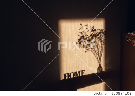 Light and shadow through the window on wall with inscription Home and dried bouquet in transparent vase Light and shadow through the window on wall with inscription Home and dried bouquet in transparent vase 130854102