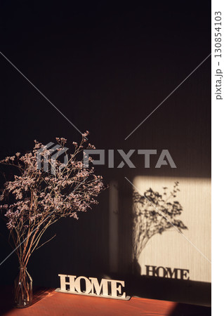 Light and shadow through the window on wall with inscription Home and dried bouquet in transparent vase 130854103