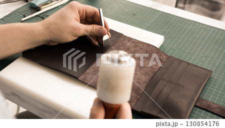 Leather crafting process with awl and mallet while making handmade wallet on workbench 130854176