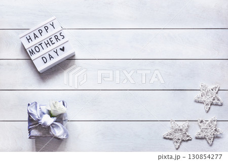 Gift box trendy wrapped in silk fabric in Furoshiki technique, white flower Eustoma or Lisianthus, light box with lettering Happy Mother's Day on wooden background Gift box trendy wrapped in silk fabric in Furoshiki technique, white flower Eustoma or Lisianthus, light box with lettering Happy Mother's Day on wooden background 130854277